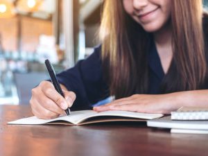 Closeup image of a business woman writing on blank notebook on wooden table