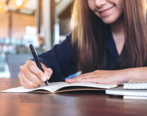 Closeup image of a business woman writing on blank notebook on wooden table