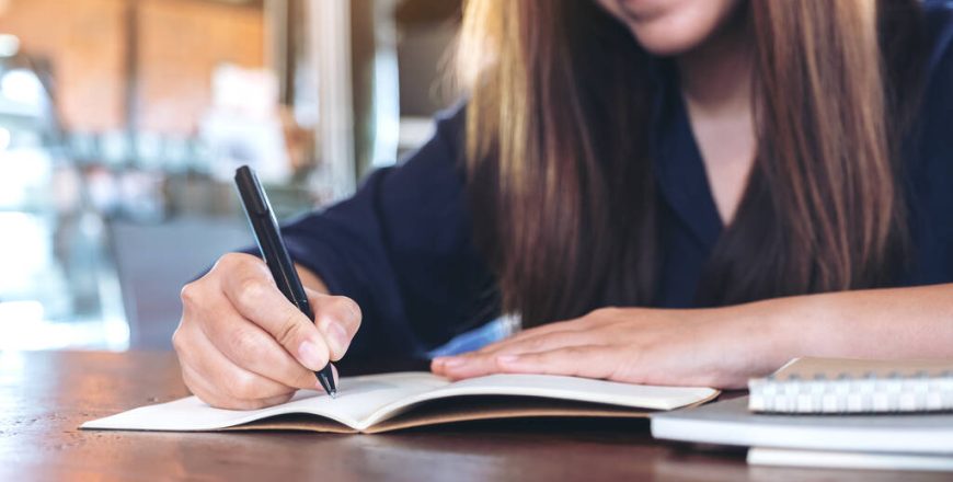 Closeup image of a business woman writing on blank notebook on w