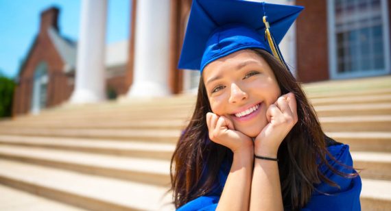 Young college girl in cap and gown having her portrait taken on the steps of college campus